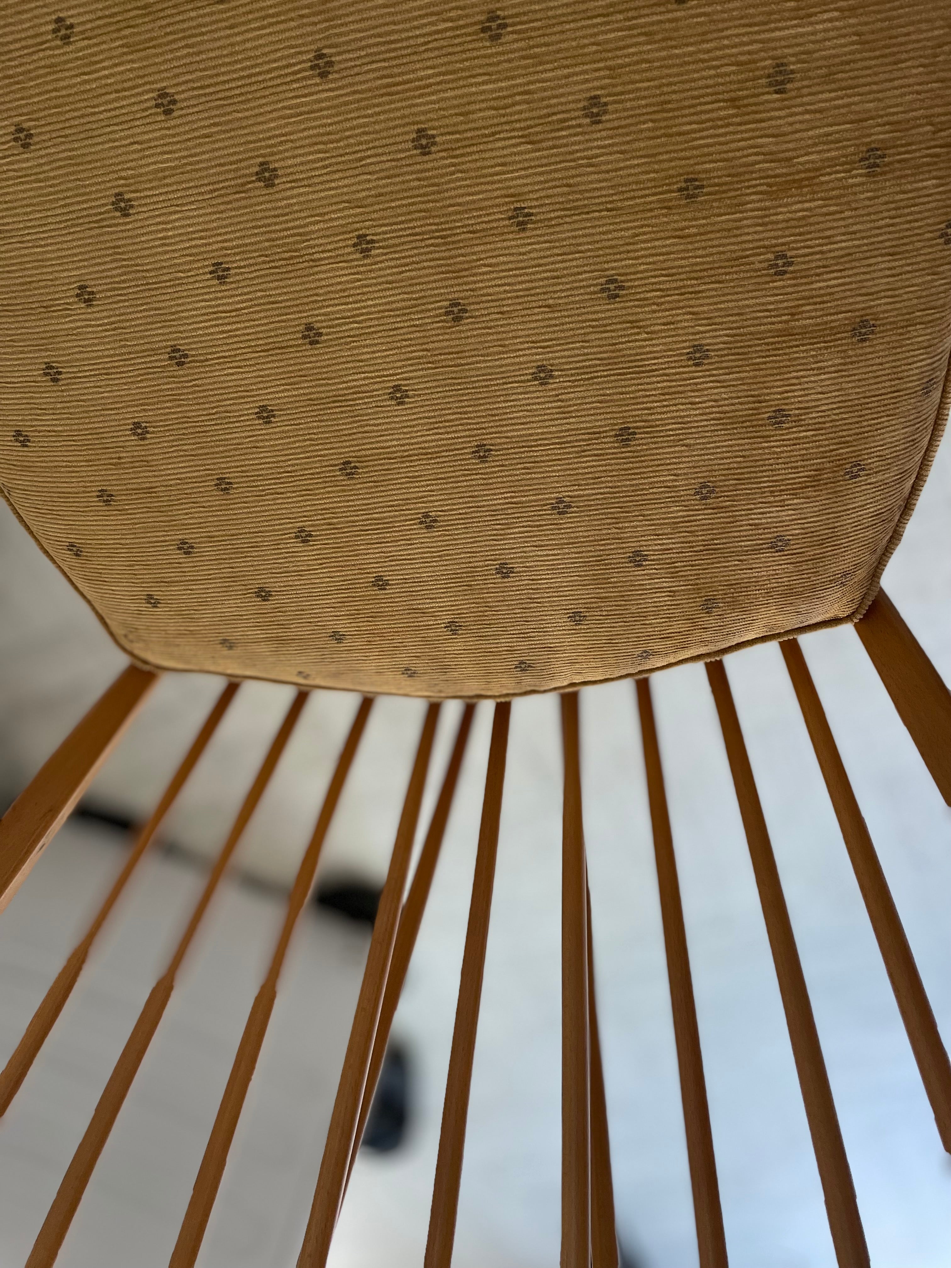 Close-up of a Ercol high back grandfather chair with a mustard foam seat on a light wooden floor.