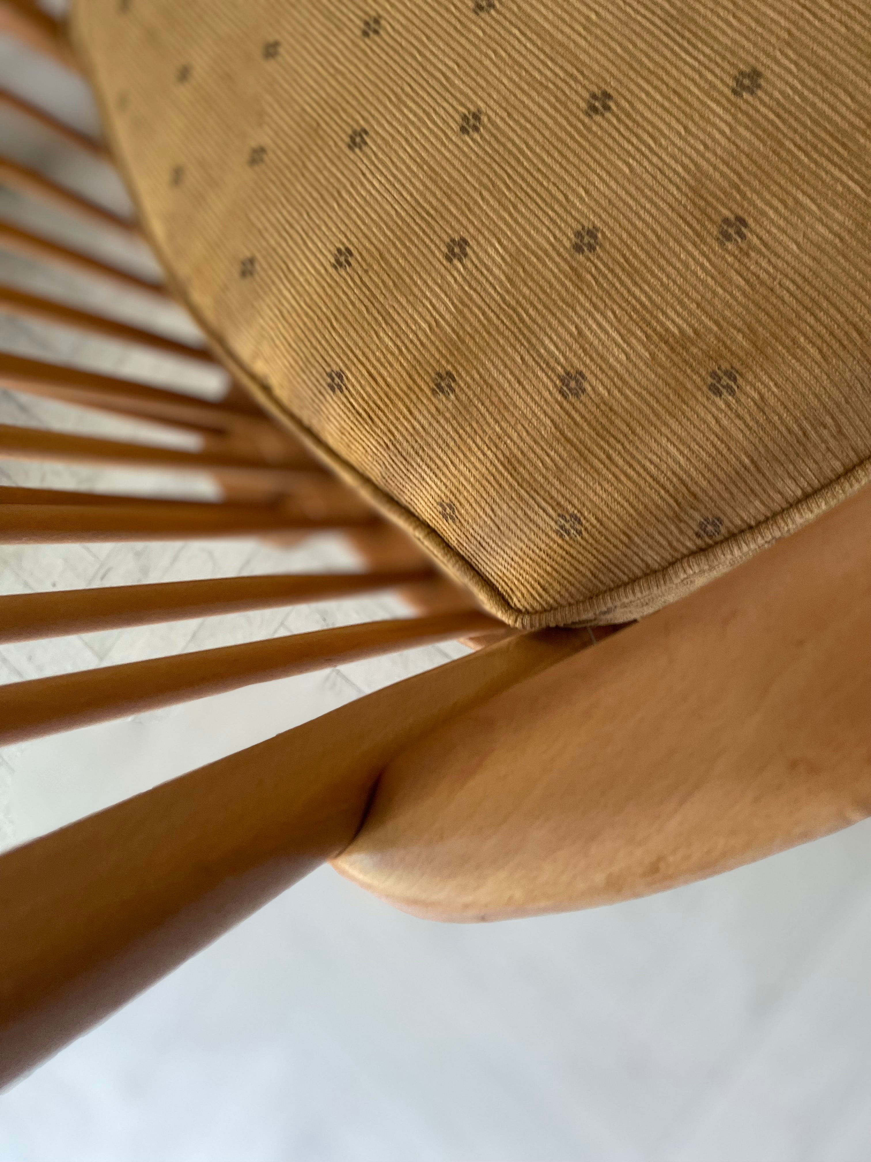 Close-up of an Ercol Elm and beech armchair with a textured mustard upholstery on a white background