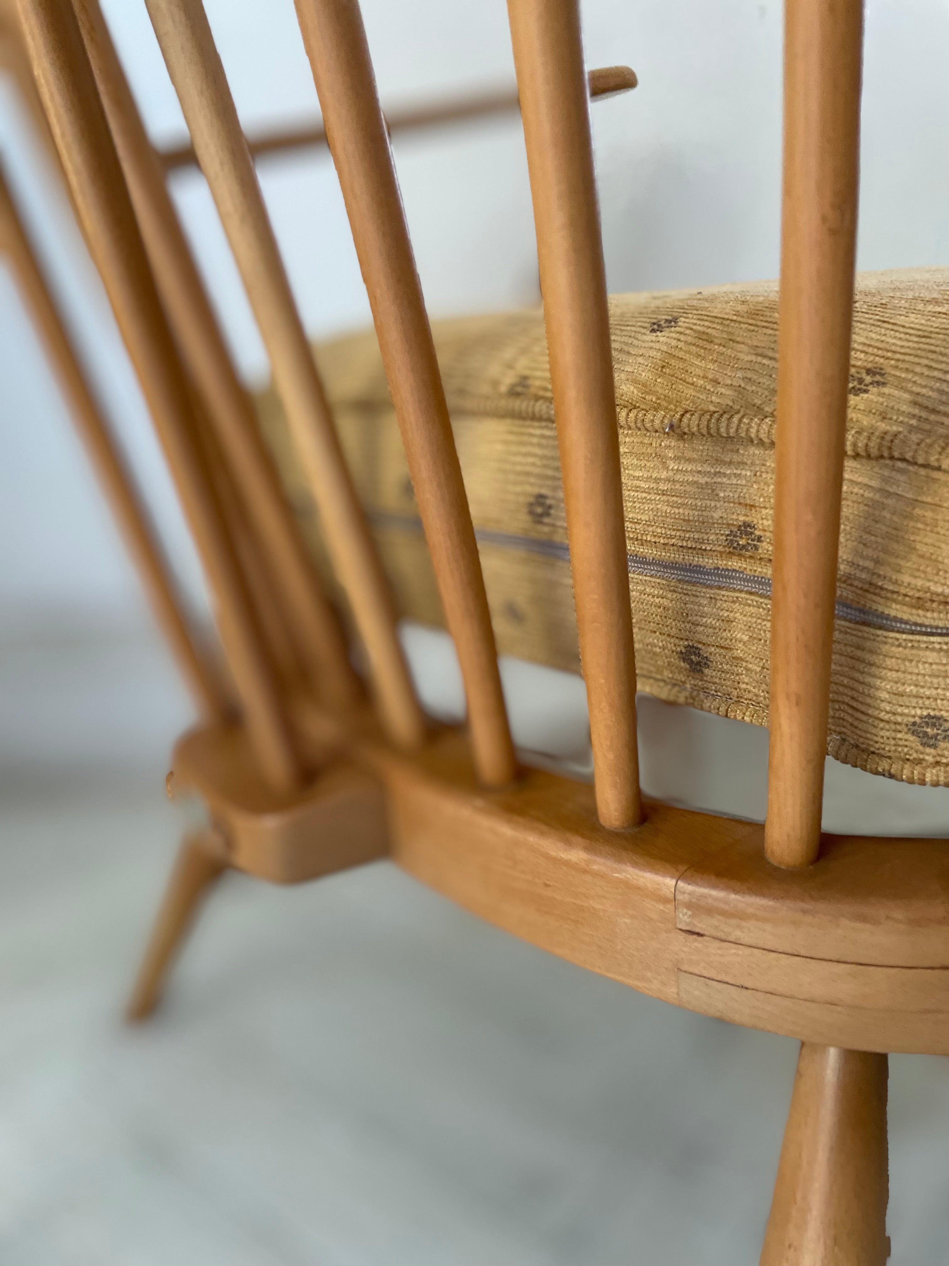 Close-up of a wooden Ercol high back armchair with a woven mustard seat on a light background
