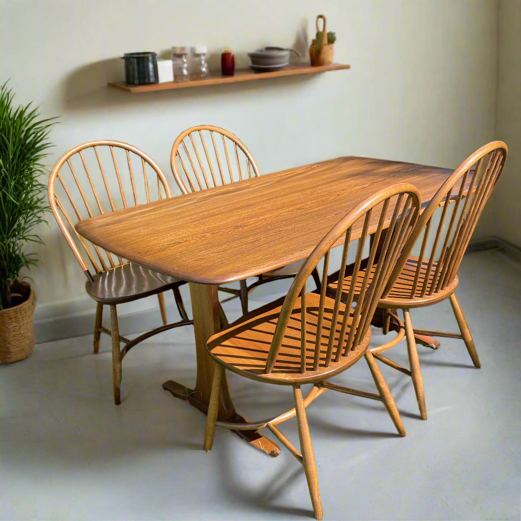 Ercol elm Wooden dining table with four chairs in a room with a shelf and plant.