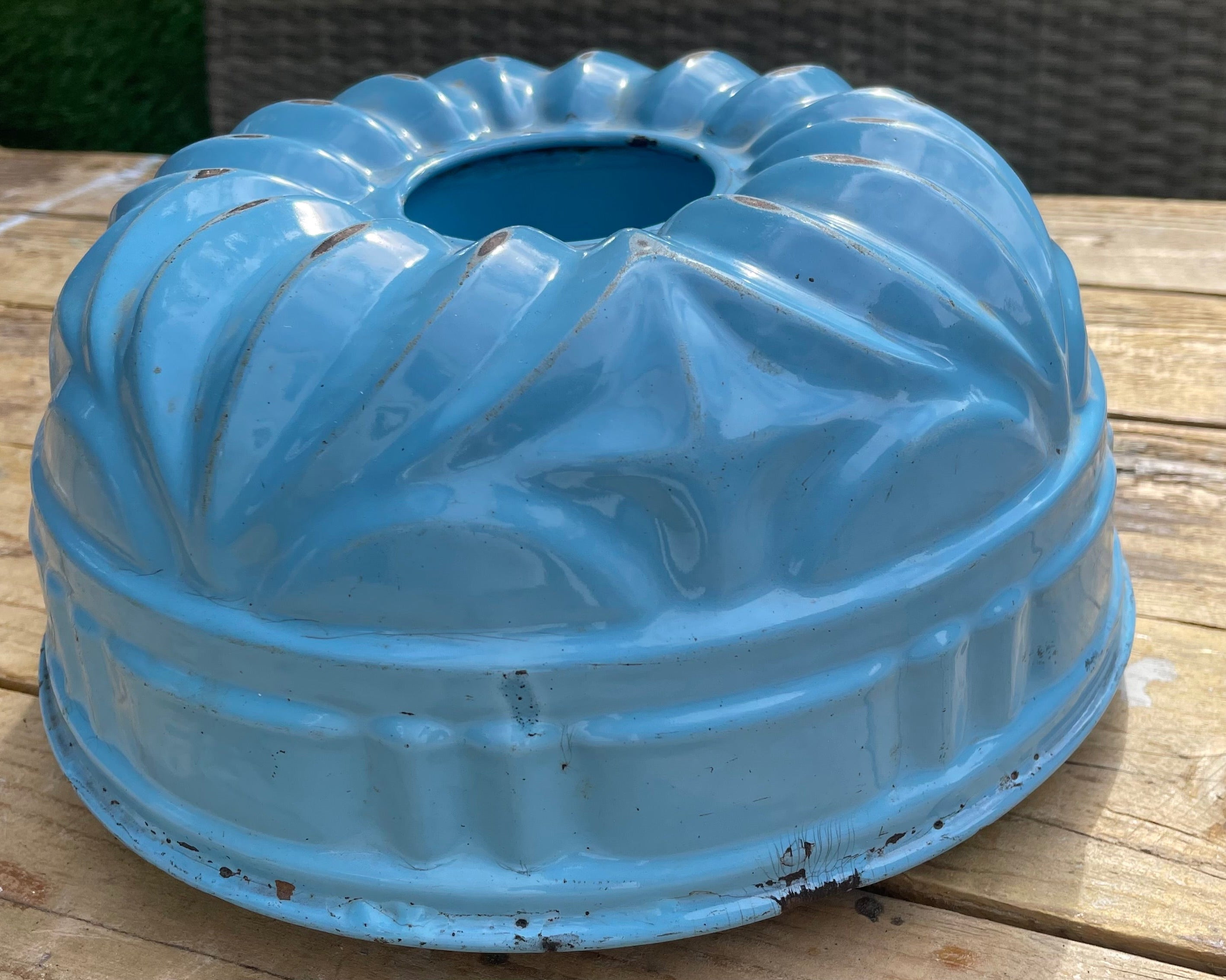  light blue fluted metal bundt cake pan with a distressed, vintage finish, sitting on a rustic wooden table.
Details
