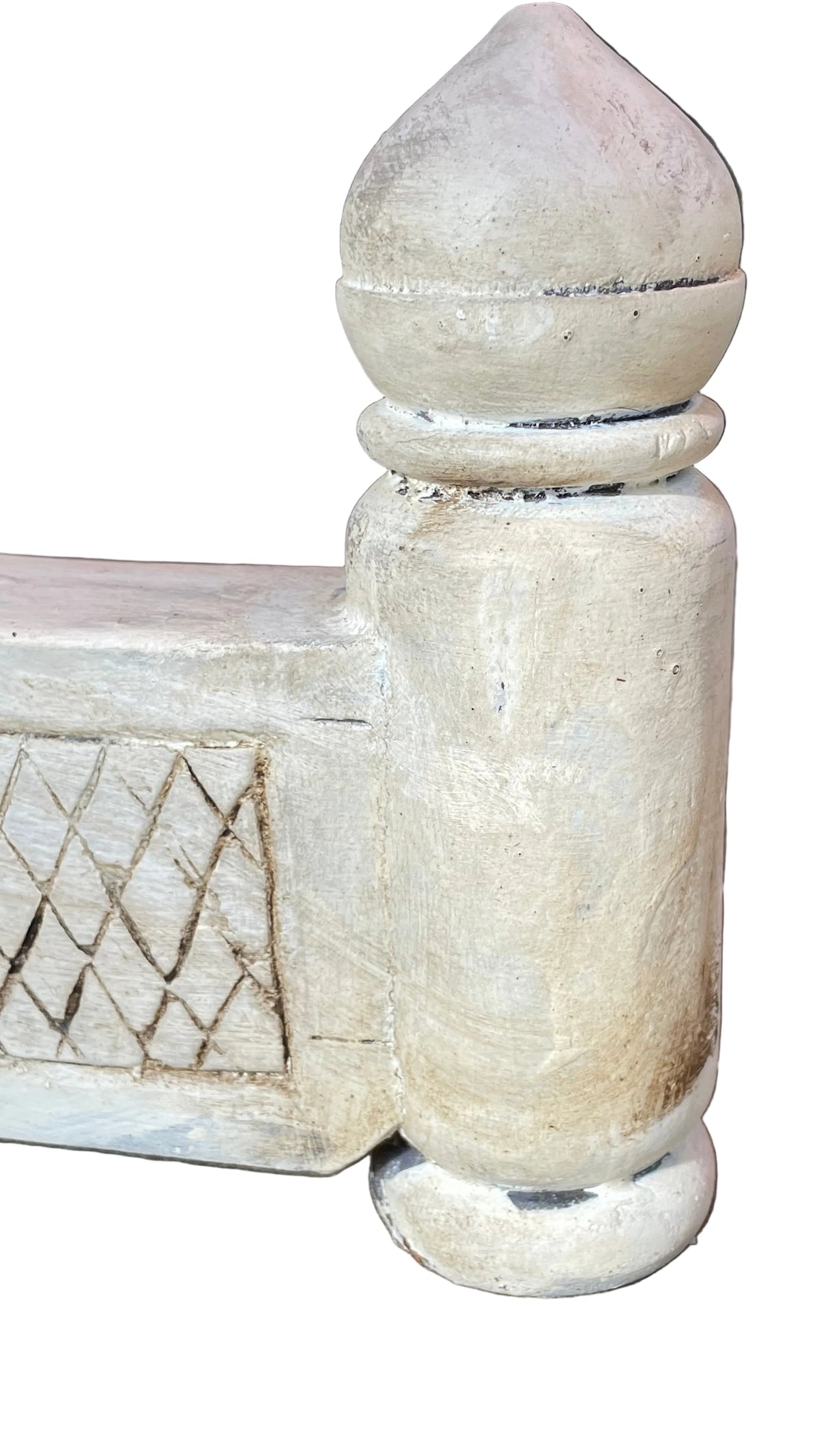 close-up of a distressed, light beige painted wooden bed frame post with a decorative diamond pattern on the side rail, set on a concrete floor