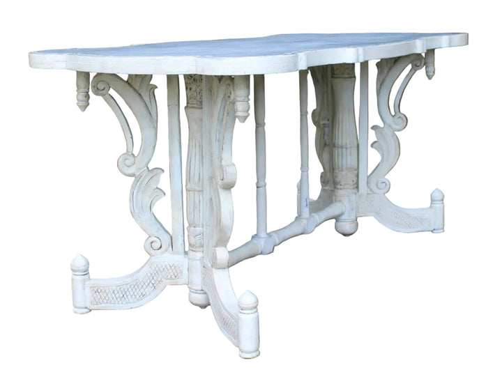 A white ornate outdoor dining table with a scalloped top and decorative pedestal legs