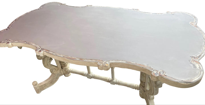 A distressed white Continental dining table with a scalloped edge and ornate legs