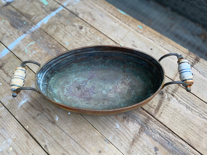 rustic copper-colored metal bowl with a curved handle and small feet
