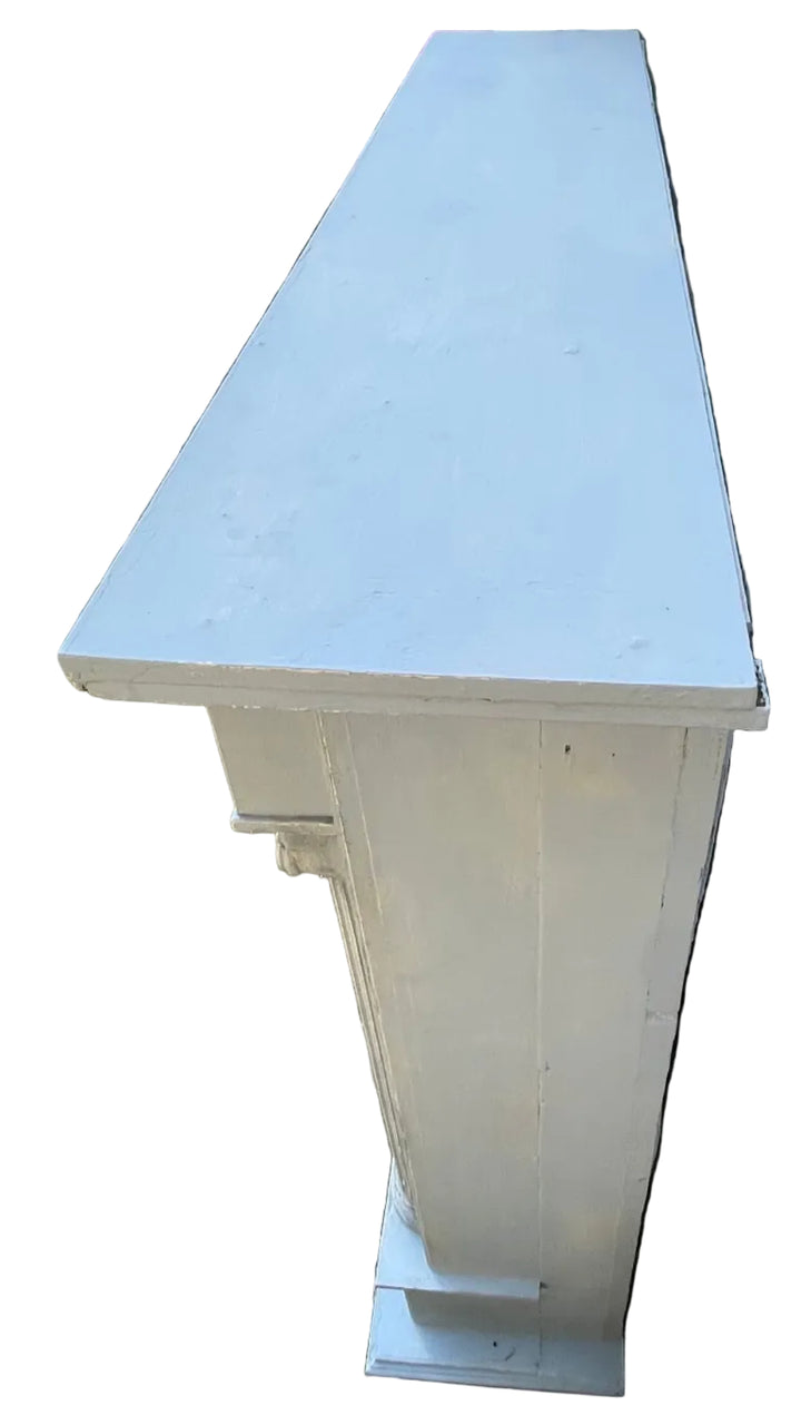 A tall, narrow white wooden cabinet or storage unit with a flat top, photographed outdoors on a paved patio next to a textured wall.