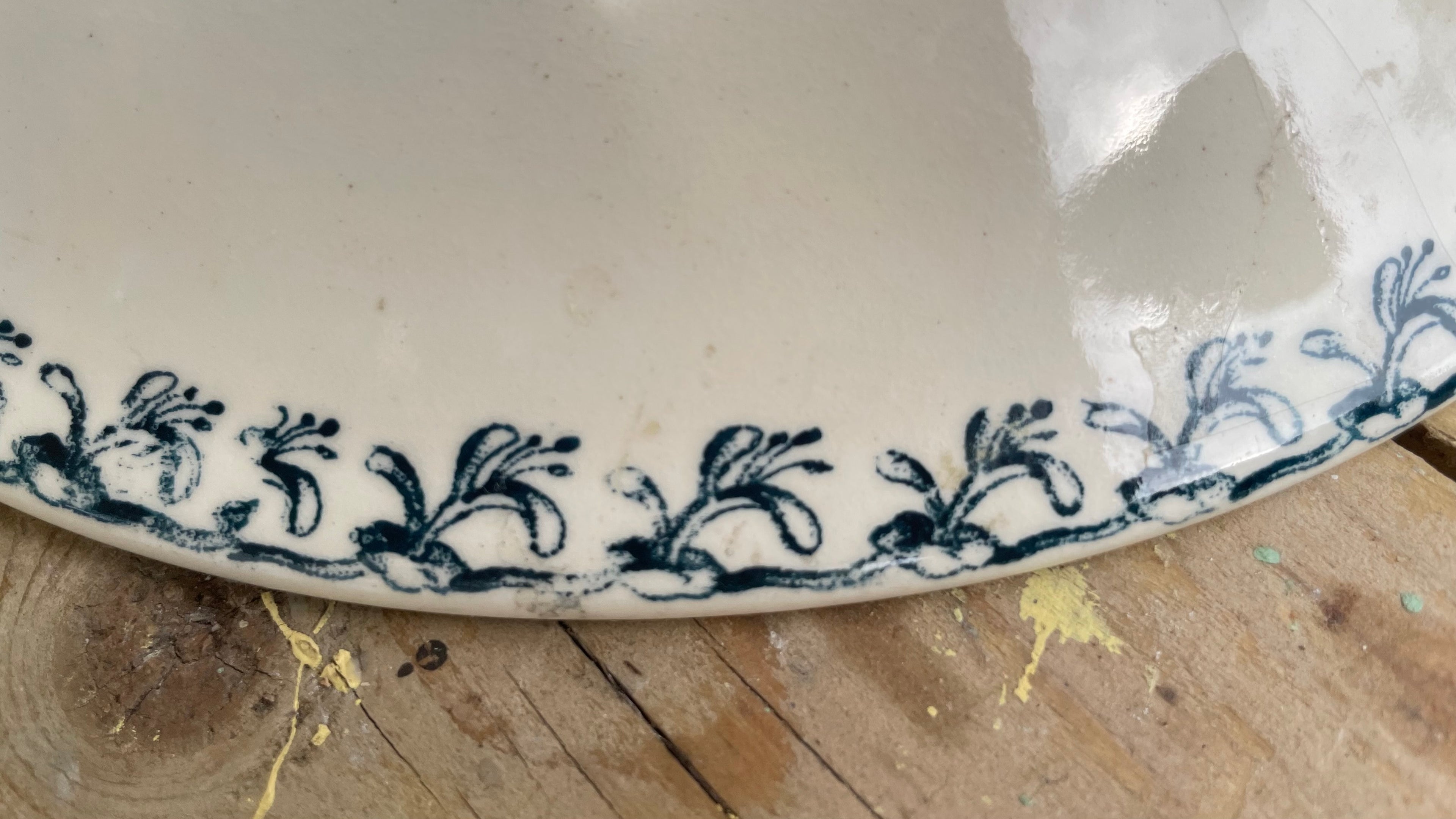 A close-up of a white ceramic plate with a blue floral border pattern, resting on a rustic wooden surface.