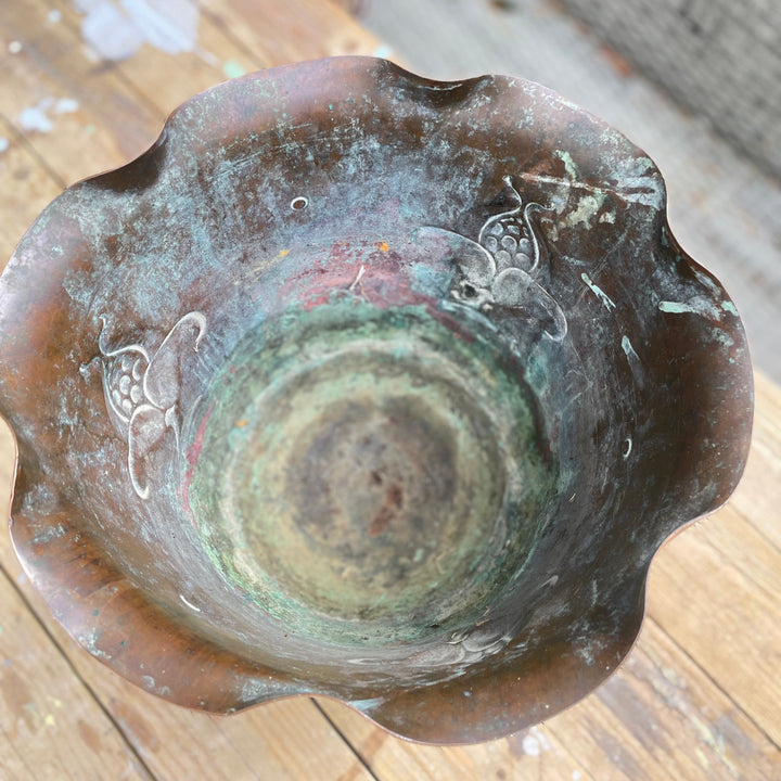 An antique bronze-coloredcerami bowl with a scalloped rim, featuring a green patina and white painted floral details, shown from a top-down perspective.