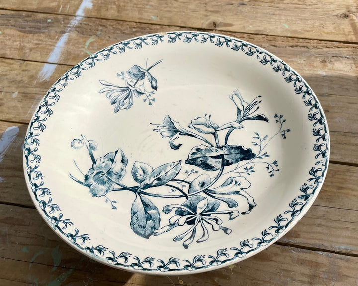 A round ceramic serving bowl with a blue floral and butterfly pattern on a cream-colored glaze, set on a rustic wooden plank surface.