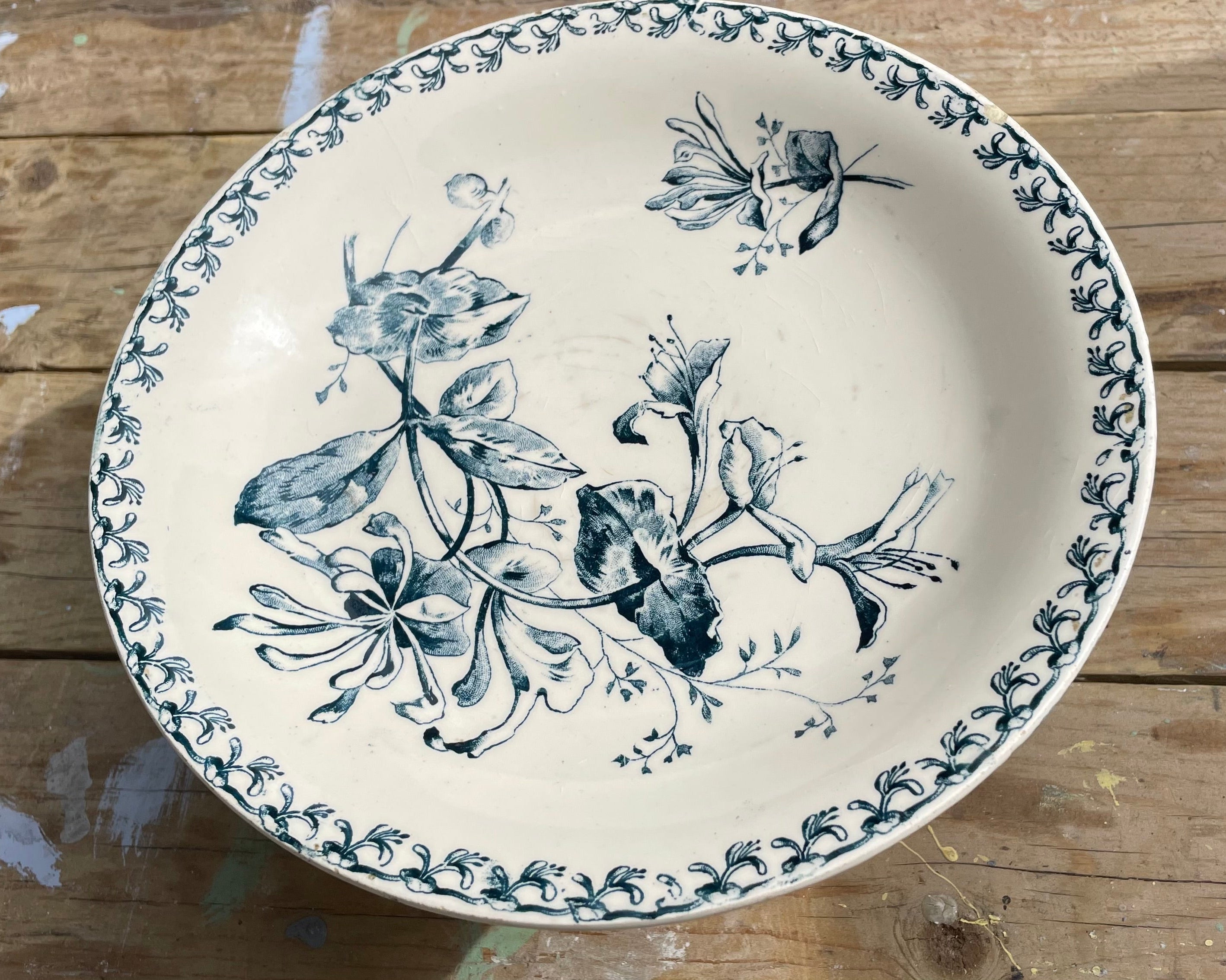 A round ceramic fruit bowl with a blue floral and butterfly pattern on a cream-colored glaze, set on a rustic wooden surface. Available for purchase from vintagemidcentury.co.uk

