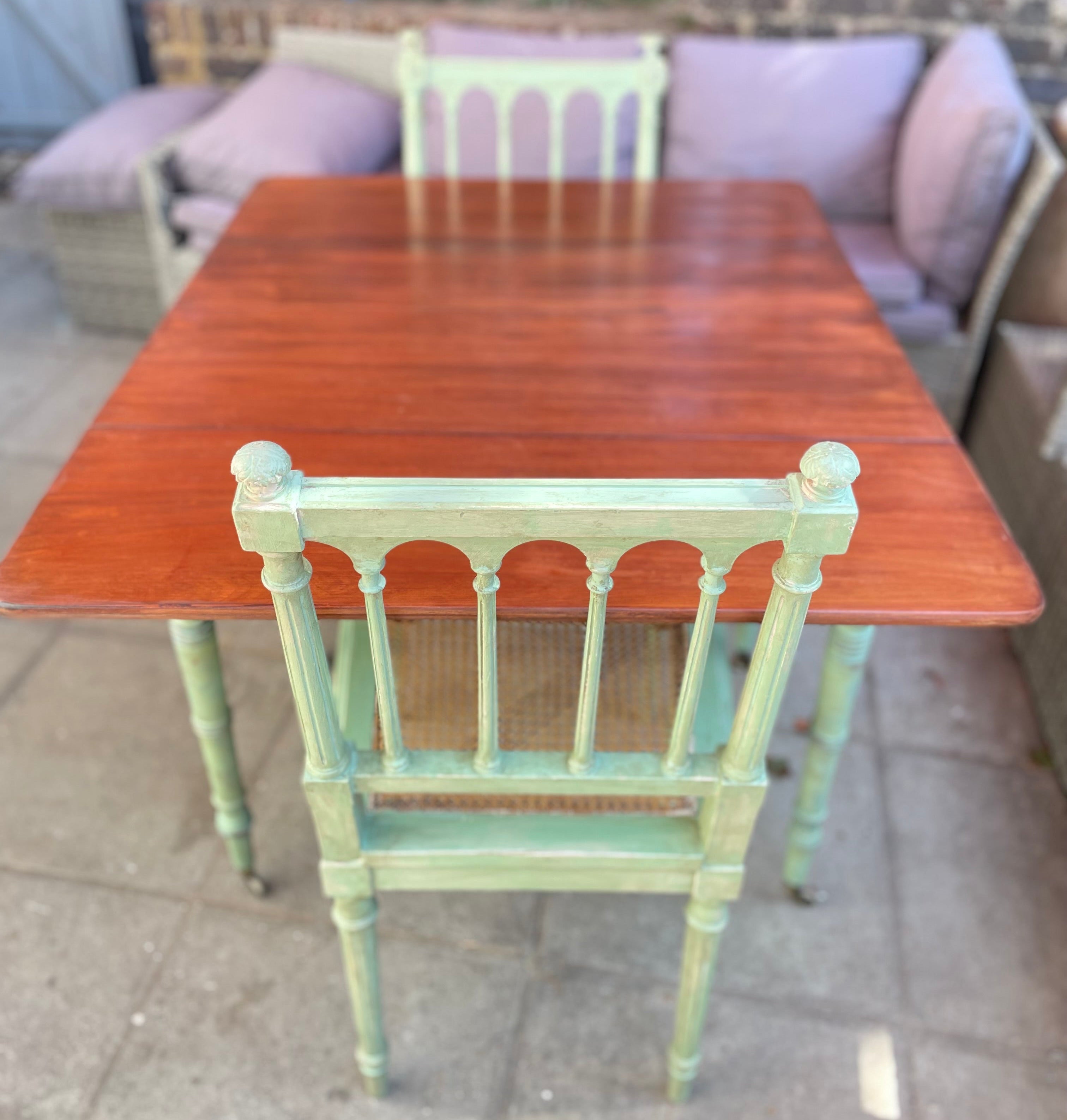 rustic wooden dining table with a reddish-brown finish, paired with distressed sage green chairs