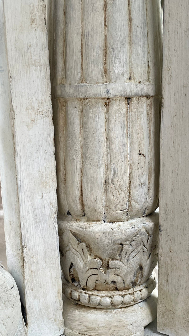 Close-up of a weathered, light-colored carved wooden column with vertical fluting and a decorative capital, surrounded by matching wooden beam