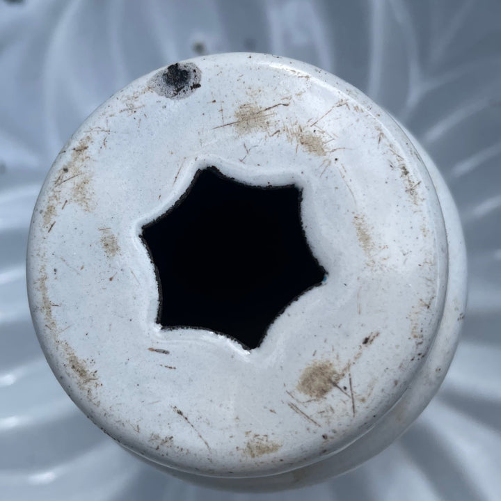 close-up top-down view of a white plastic bottle cap with a six-point star socket opening, showing some dirt and wear, set against a matching white ribbed plastic background.