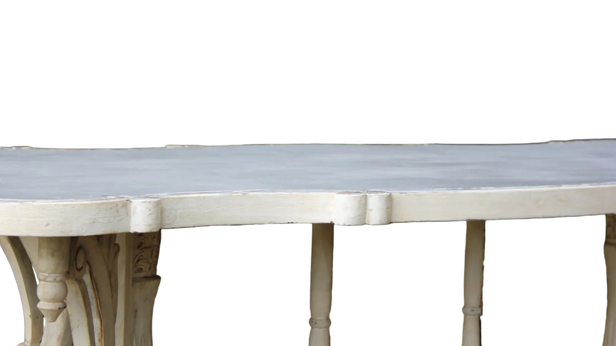 A close-up of a white painted wooden table outdoors, showing the tabletop and carved legs