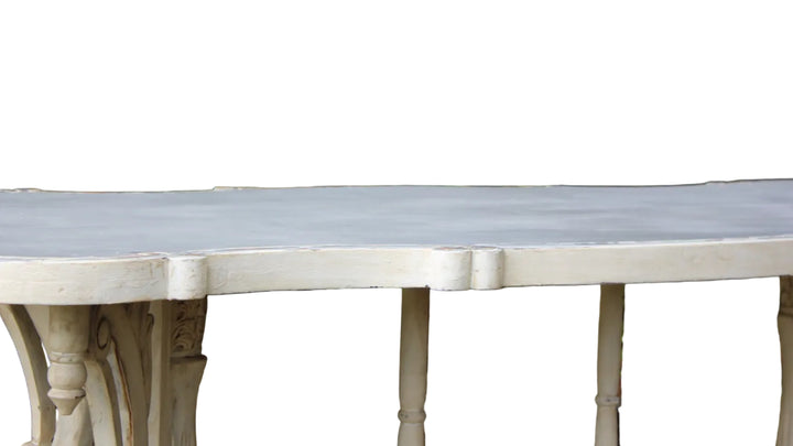 A close-up of a white painted wooden table outdoors, showing the tabletop and carved legs