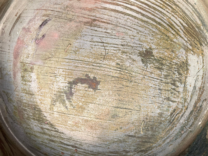 Close-up of a heavily scratched and worn metal surface, likely the inside of a pan or plate, showing rust, grime, and circular cleaning marks.