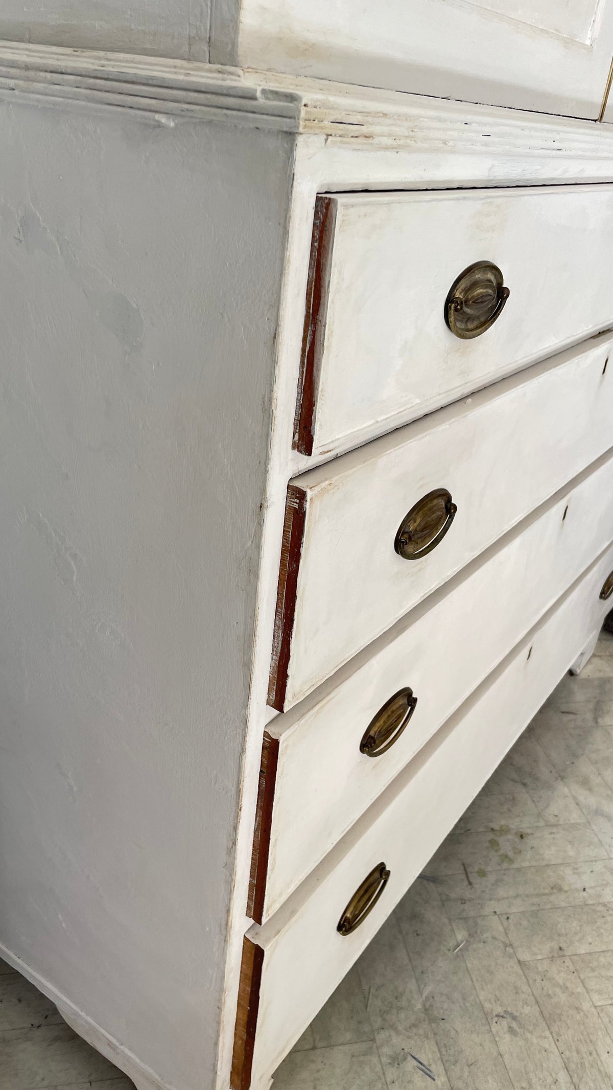 A close-up of a distressed white wooden dresser with three drawers and round brass handles, showing the chipped paint and wood grain details.