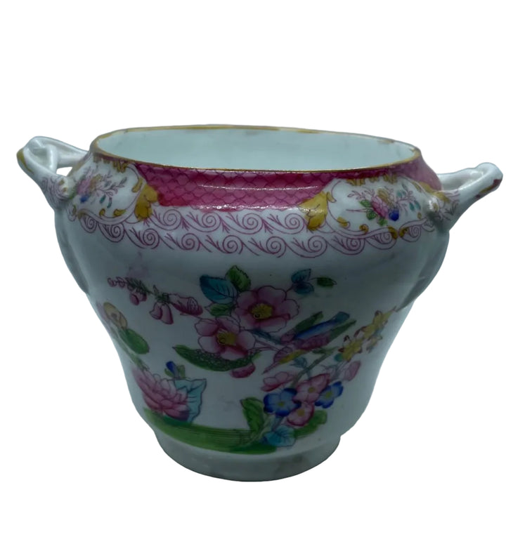 white porcelain cup with two side handles, decorated with a pink floral pattern and gold accents, set against a white backdrop.
