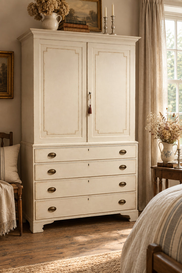 A tall, distressed off-white wooden cabinet with two upper doors and four lower drawers, featuring brass oval handles and a small hanging tassel, photographed in a home interior.