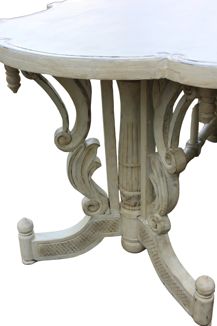 A distressed white carved wooden table with ornate scrollwork leg