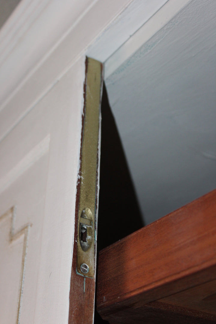 Close-up of a brass door latch and strike plate on a white panelled door of Ann Antique linen press.