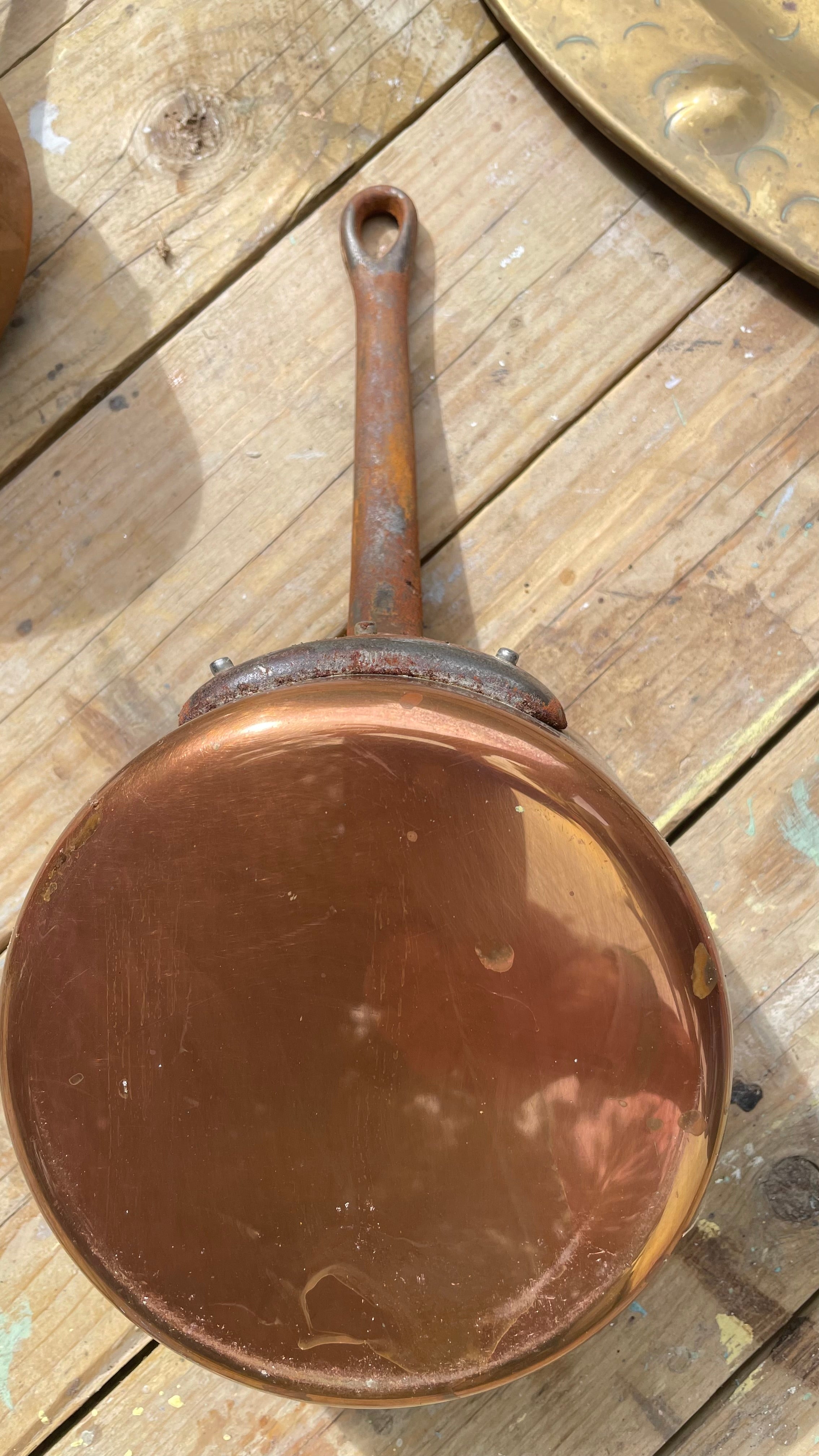 A round copper pan with a long handle, photographed from above on a rustic wooden surface.