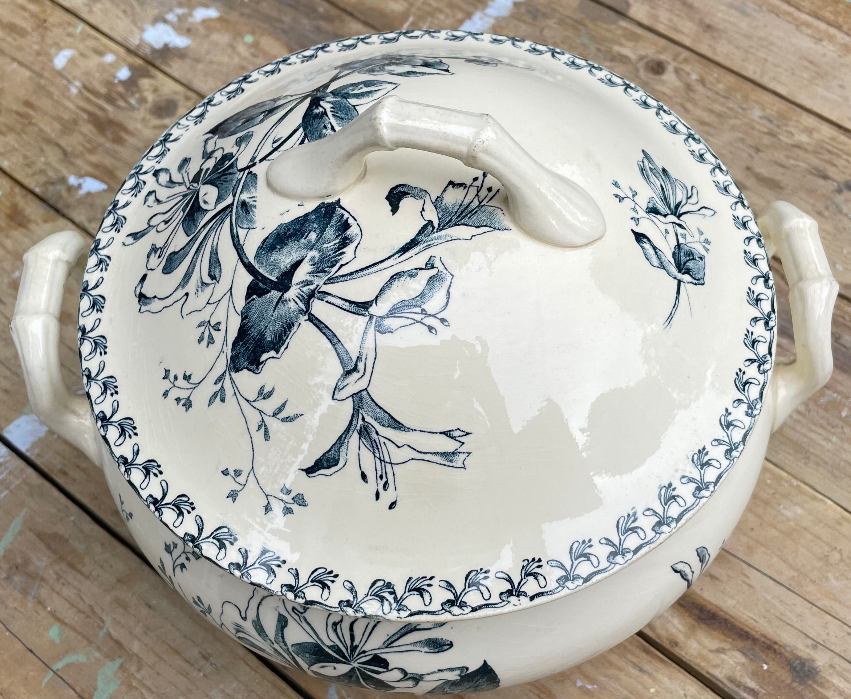 


An off-white ceramic lidded casserole dish with blue floral illustrations and side handles, resting on a rustic wooden plank surface.