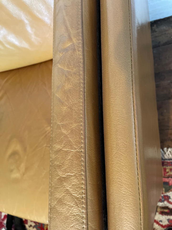 Close-up of a tan leather sofa visible stitching on a patterned antique rug in the background.