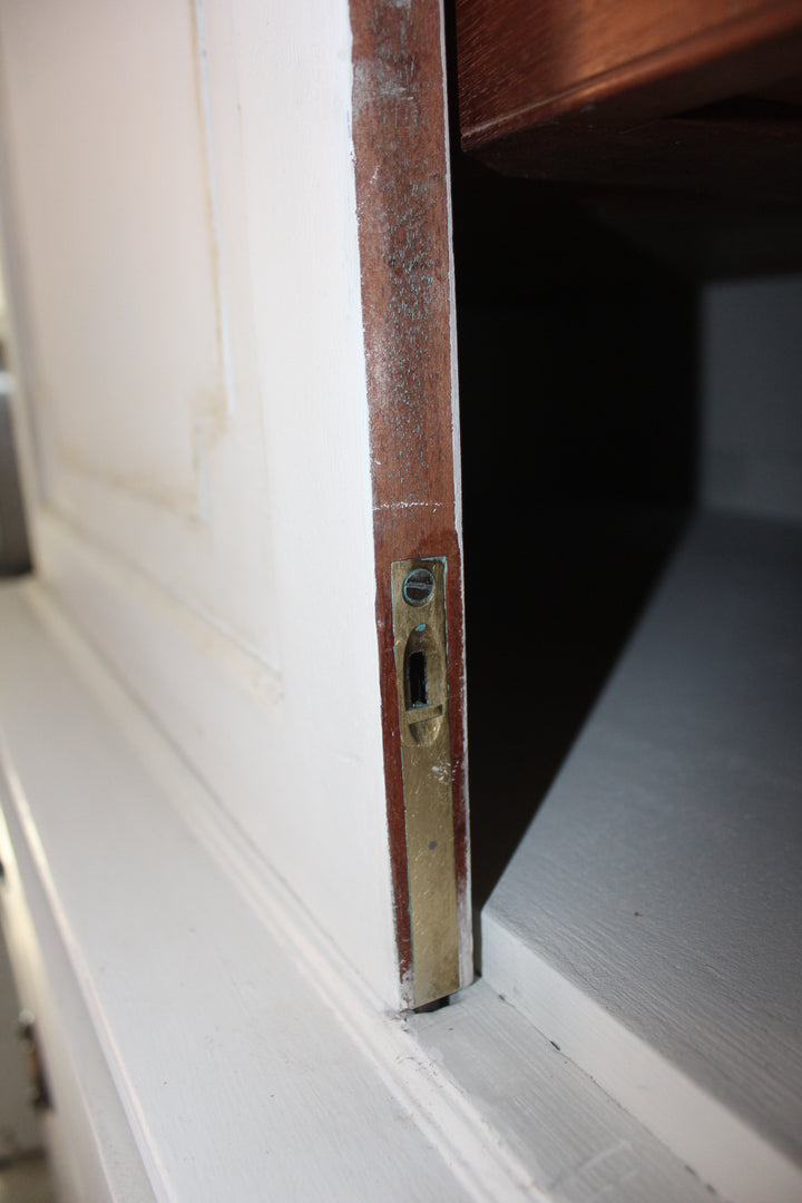 Close-up of a weathered brass cabinet latch and lockset on a white-painted wooden door frame.
