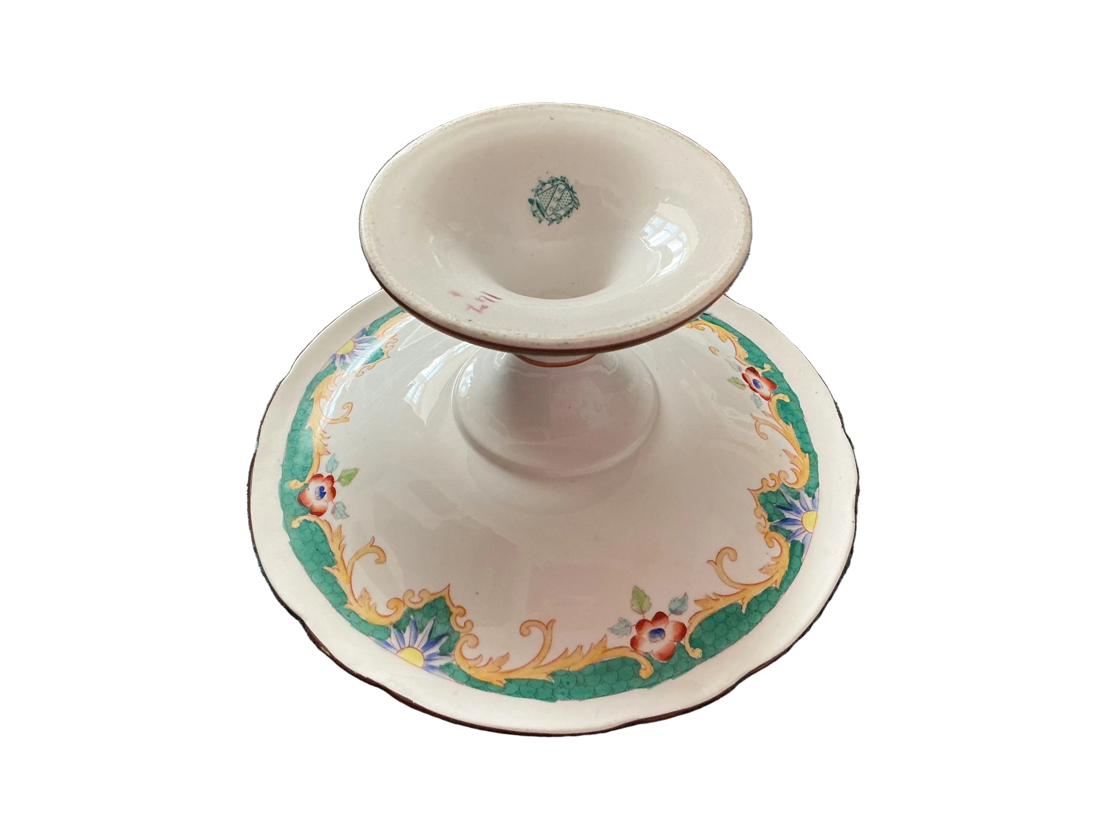vintage white porcelain candle holder with a matching saucer featuring a green, gold, and floral pattern, resting on a textured teal blanket.