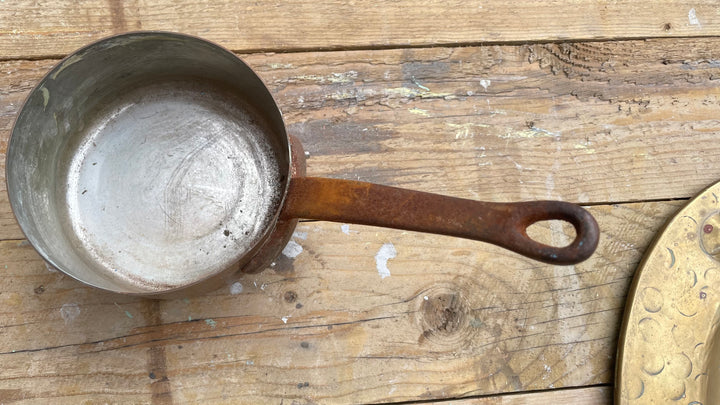 A vintage cast iron saucepan with a weathered brown handle, shown from a top-down perspective on a rustic wooden plank surface.
