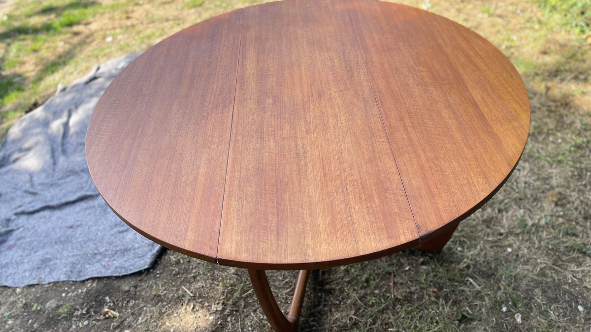 round wooden dining table with a warm reddish-brown finish and visible wood grain, photographed outdoors on grass with yard clutter in the background.
Details