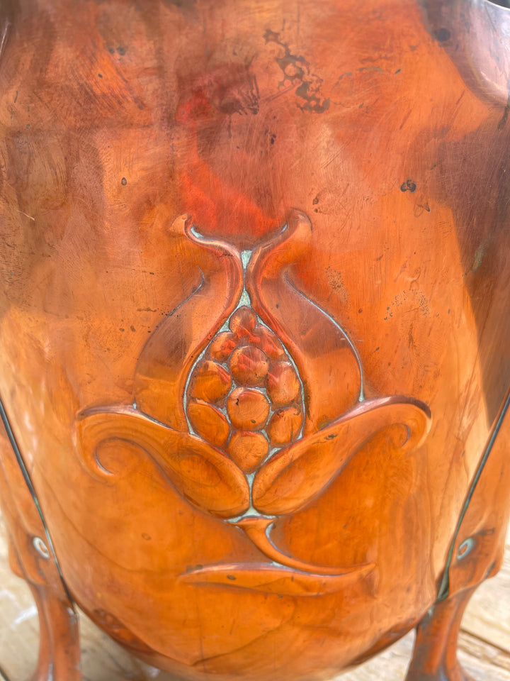 Close-up of a glossy terracotta-colored ceramic vase featuring a raised embossed floral or pomegranate-like motif on the front.