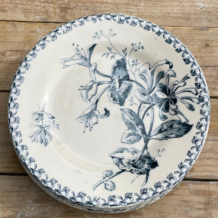 A round ceramic plate with a blue floral and botanical print on an off-white background, featuring a decorative blue patterned rim, shown on a rustic wooden plank surface.
Details