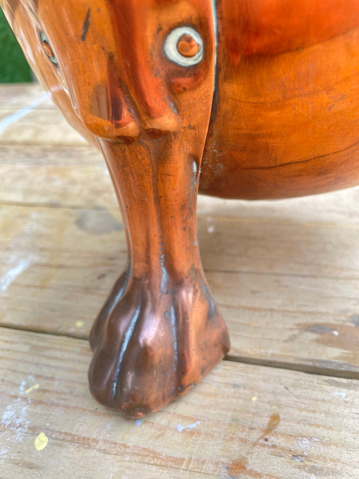 Close-up of a carved wooden leg with a glossy reddish-brown finish, resting on a light wood plank surface.