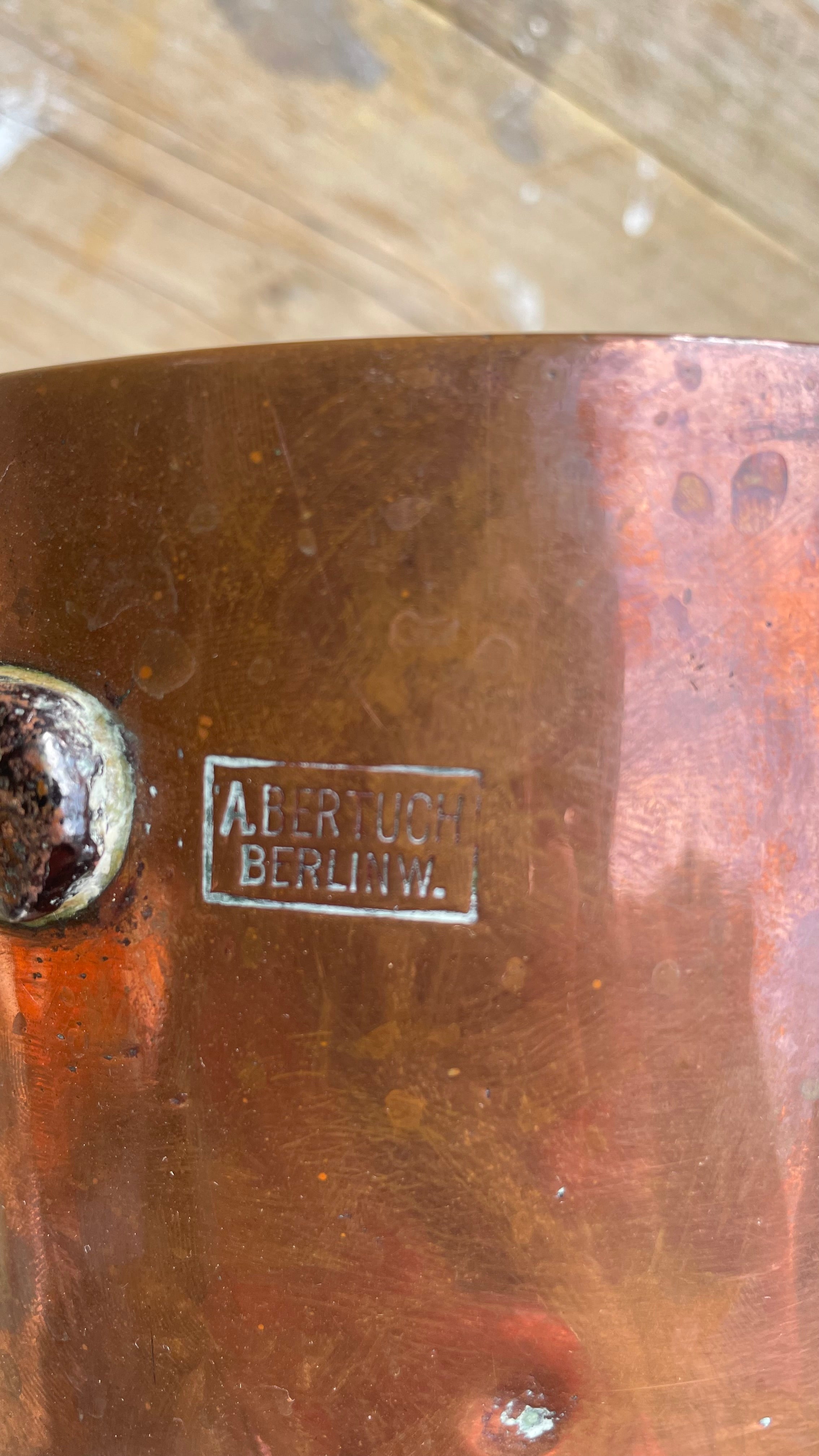 


Close-up of a copper-colored metal surface with a small rectangular stamp reading 'ABERTUCH BERLIN W.' and part of a rivet visible on the left.