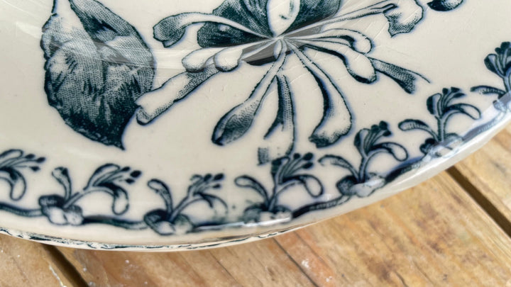Close-up of a white ceramic plate with a dark blue floral and leaf pattern, resting on a wooden surface.