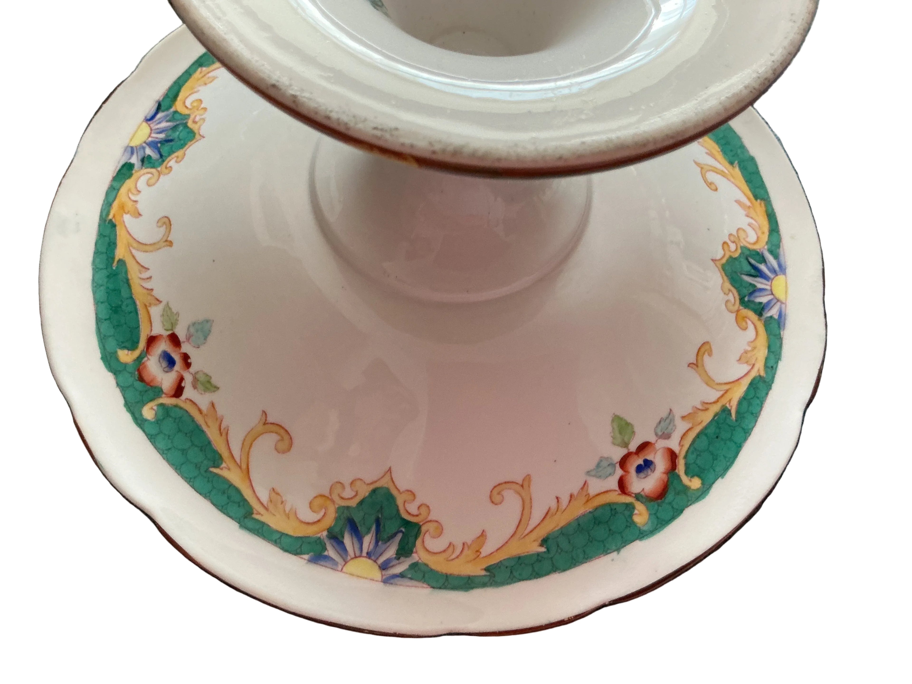vintage white ceramic pedestal plate with a scalloped rim, decorated with a green border, gold scrollwork, and small floral motifs in blue, red, and yellow.