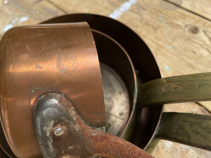 A close-up of nested copper and dark metal measuring cups with handles, resting on a rustic wooden surface.