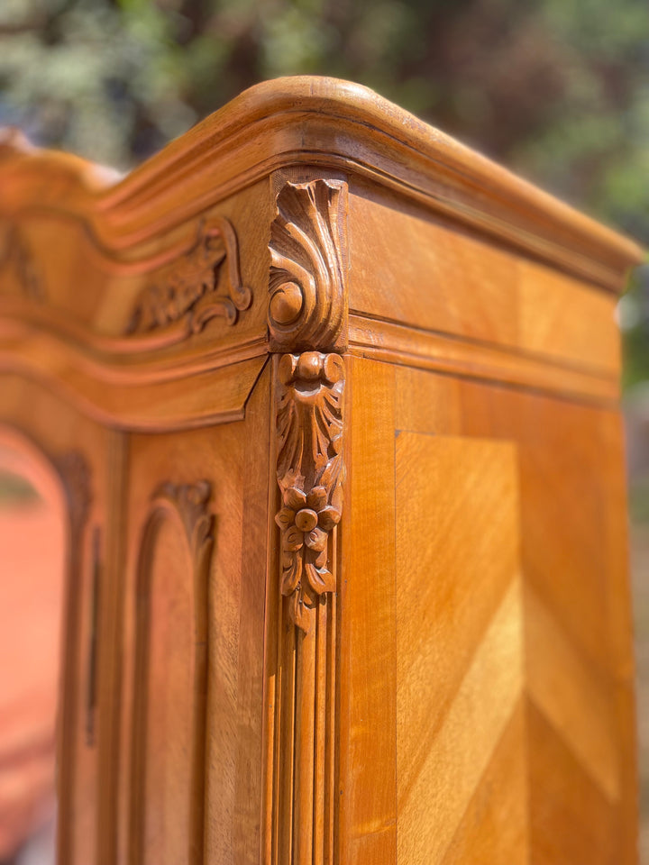 Close-up of carved floral corner detail and chevron veneer on an early 20th century French walnut mirrored wardrobe