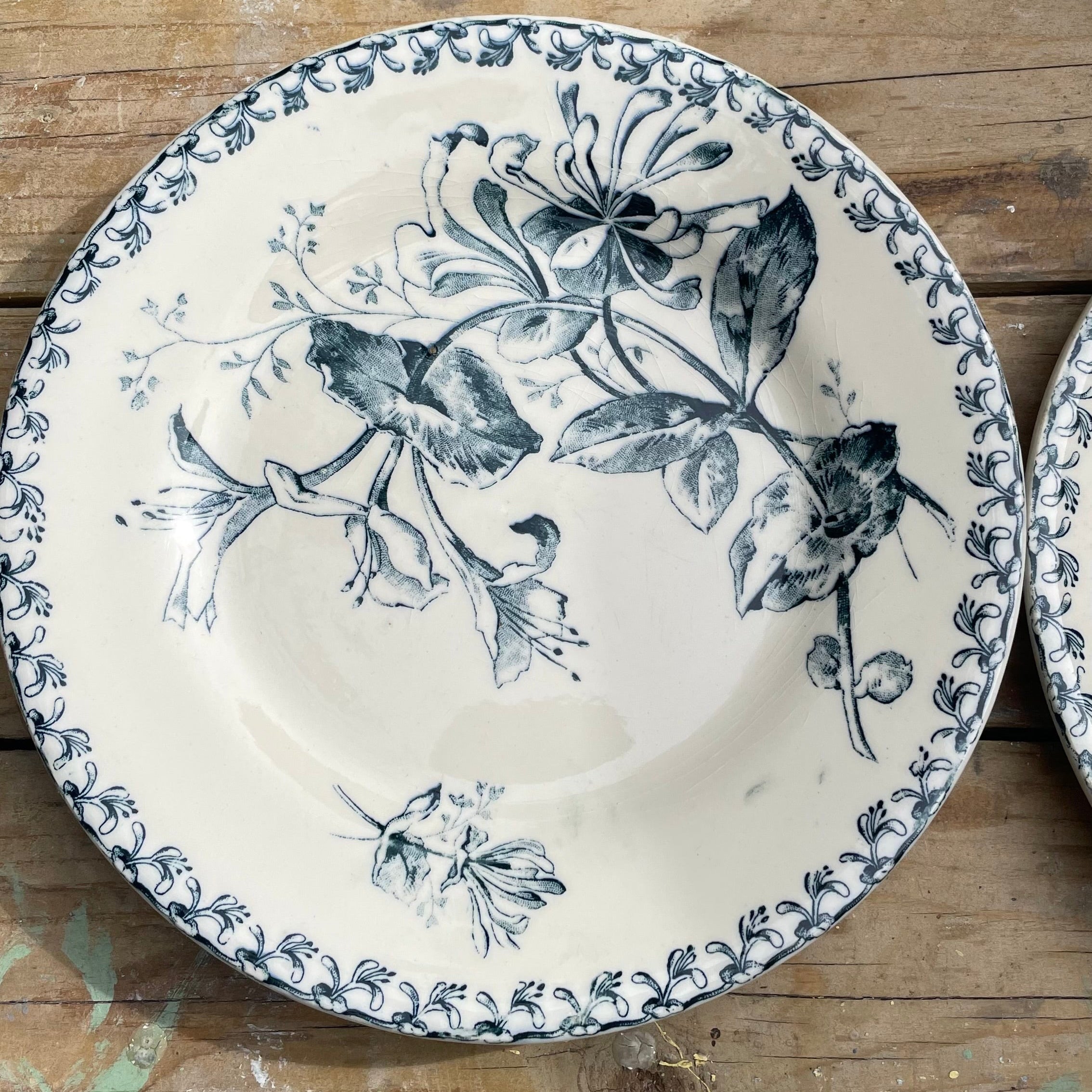 A round ceramic plate with a blue floral and bird pattern on a cream background, placed on a rustic wooden surface.
