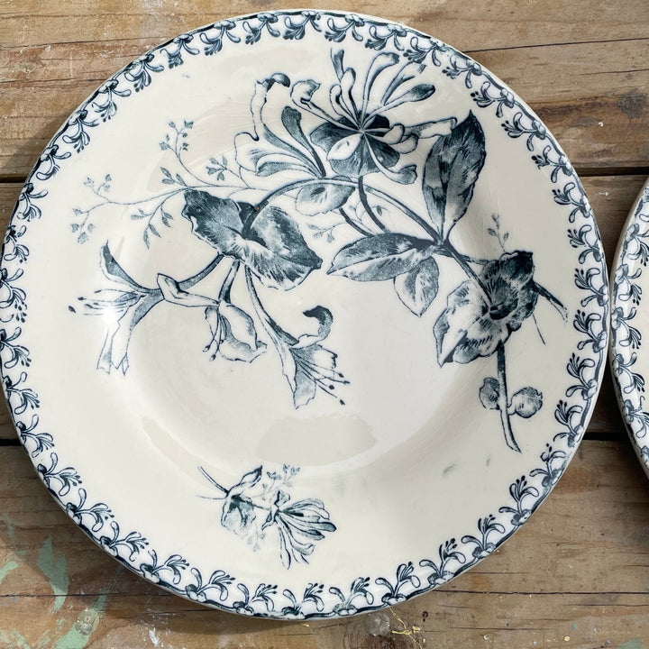 A round ceramic plate with a blue floral and bird pattern on a cream background, placed on a rustic wooden surface.
