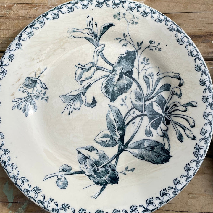 round ceramic plate with a blue floral and botanical print on a cream-colored glaze, displayed on a rustic wooden surface.