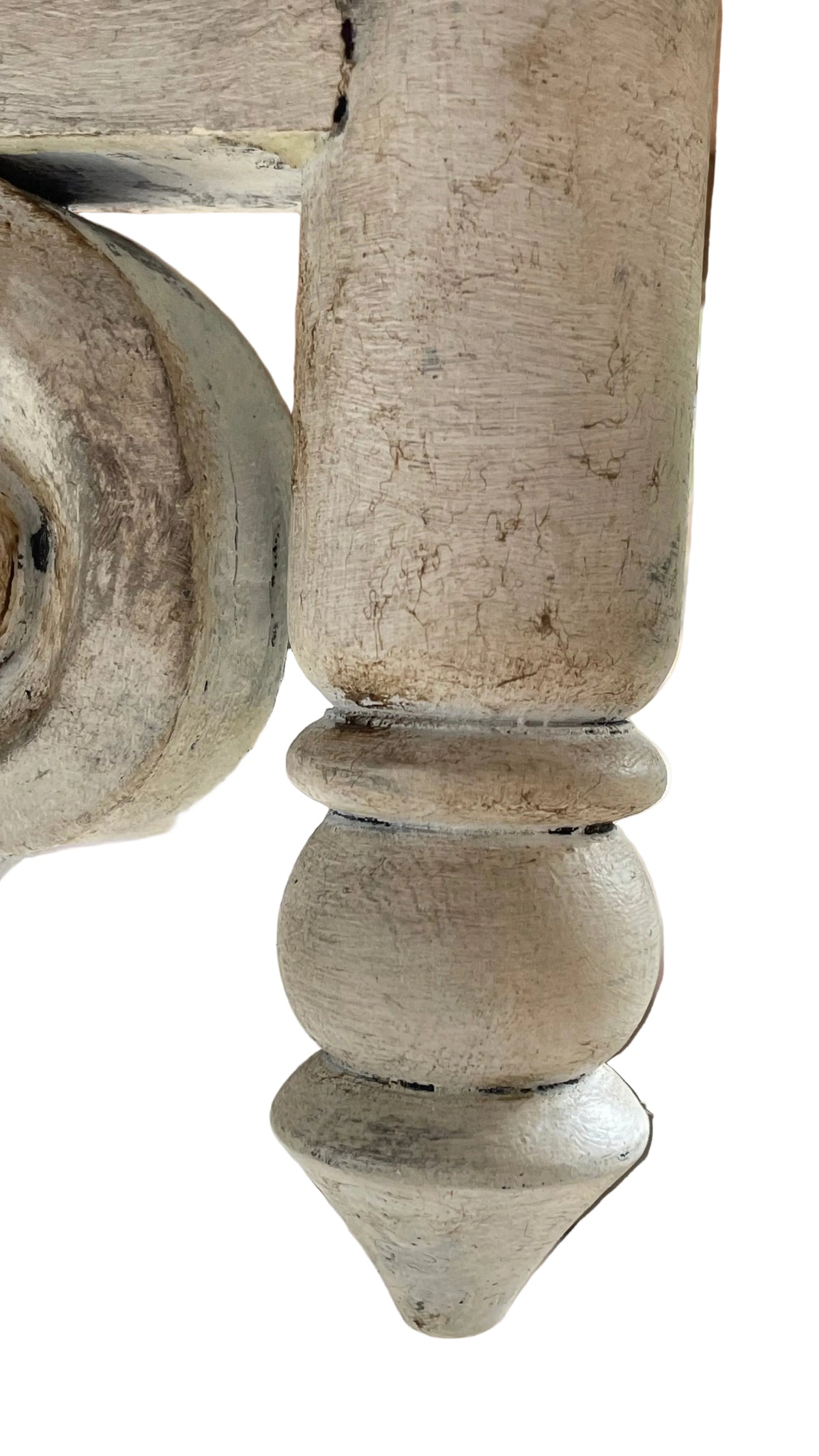 A close-up of a distressed, light beige painted wooden furniture leg with a turned ball and conical foot, showing weathered texture and chipped paint.