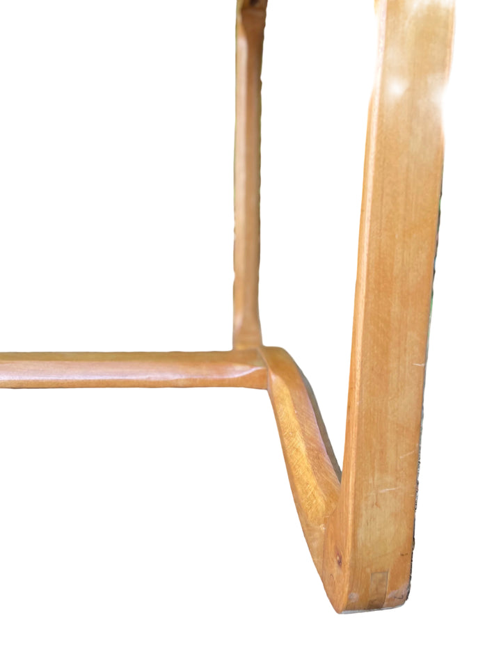 Close-up of a light Ercol 513 brown wooden table leg outdoors on dirt with blurred green foliage in the background