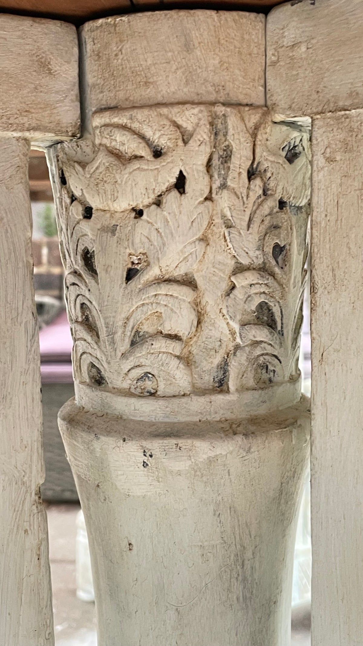 Close-up of a carved wooden table leg or pedestal with ornate floral relief detailing and a smooth cylindrical base, shown in warm natural light.