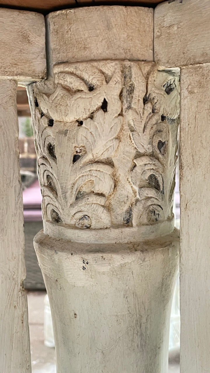 Close-up of a carved wooden table leg or pedestal with ornate floral relief detailing and a smooth cylindrical base, shown in warm natural light.