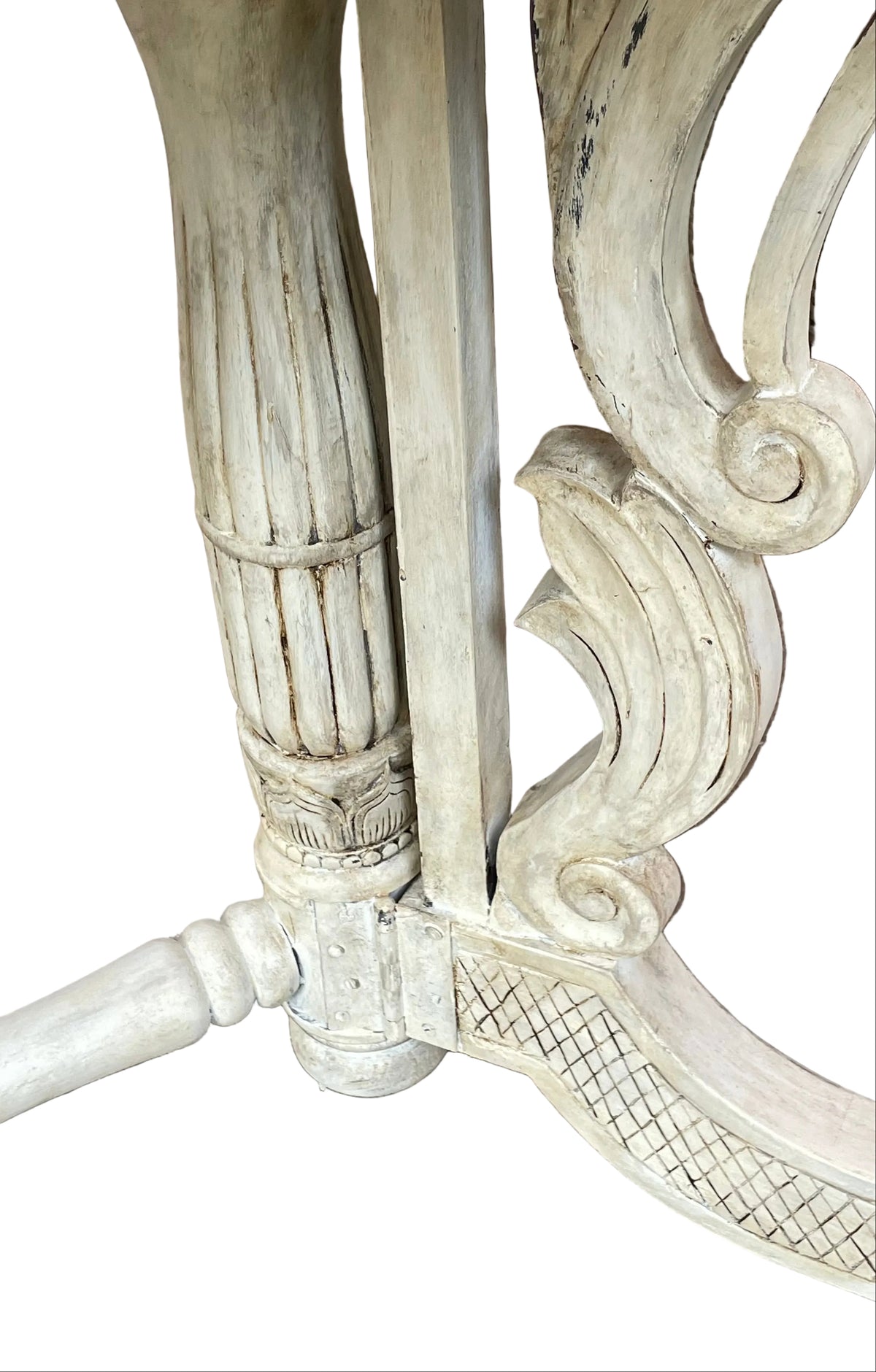Close-up detail of an ornate distressed white carved wooden table leg joint, showing decorative scrollwork and a fluted vertical post on a white background.
Details