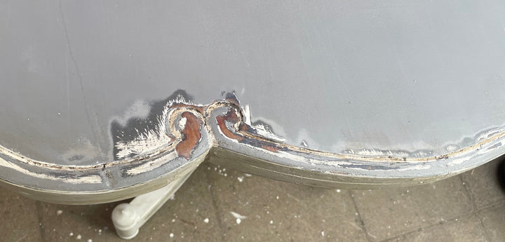 Close-up of a damaged metallic surface with heavy rust and chipped paint along a seam, photographed outdoors on a concrete floor.