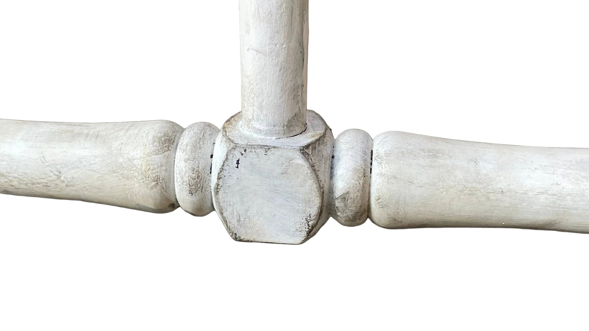 A close-up of a distressed white painted wooden table leg joint, showing the hexagonal center cap and turned spindles on a tiled floor.